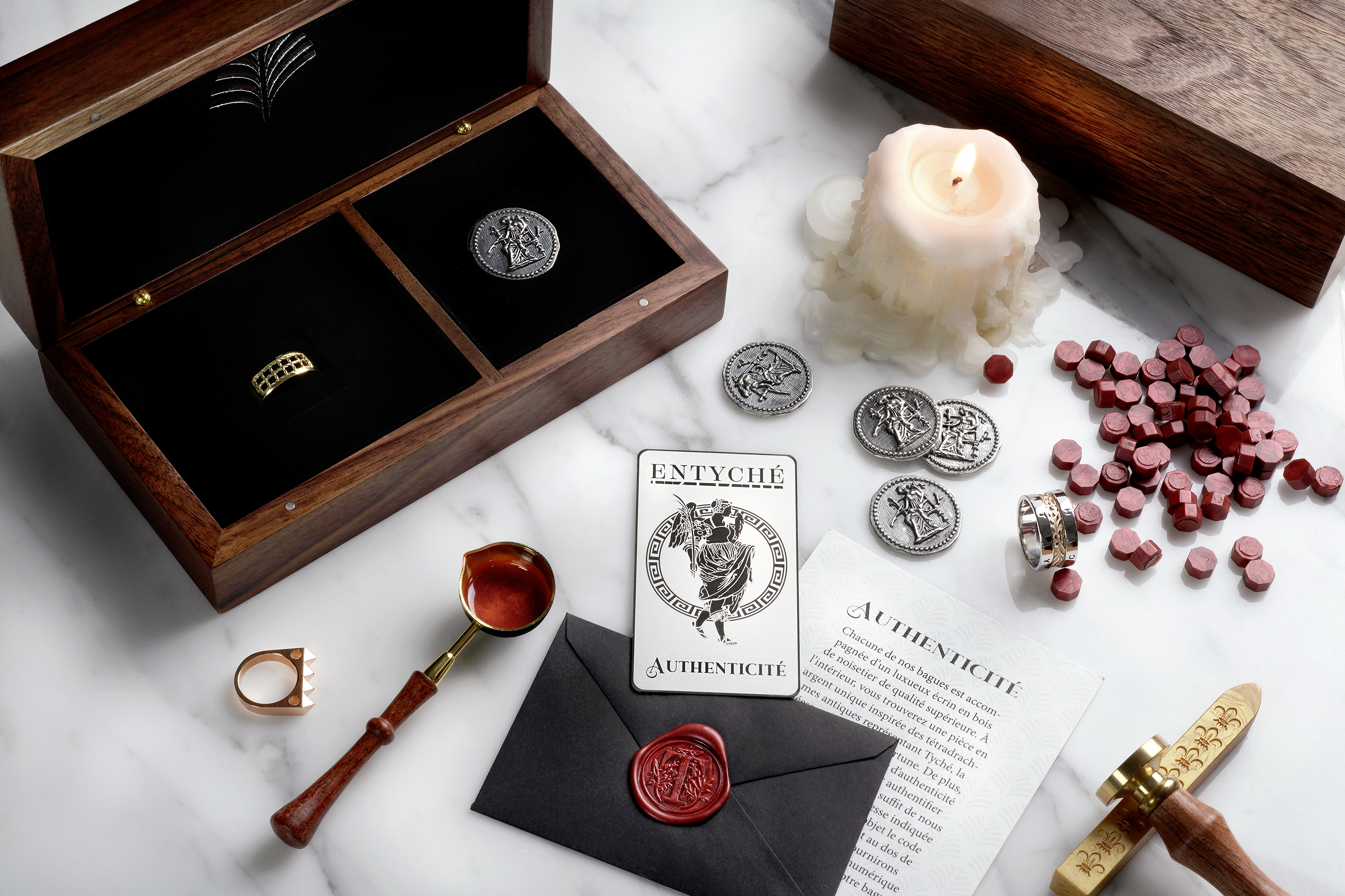 Entyché wooden box containing our Venture 14k gold ring and our signature coin. Laid in front of the box are our Tamkeen 14k rose gold ring, our Cambiante 14k gold and silver ring, our metal authenticity card as well as other packaging materials.